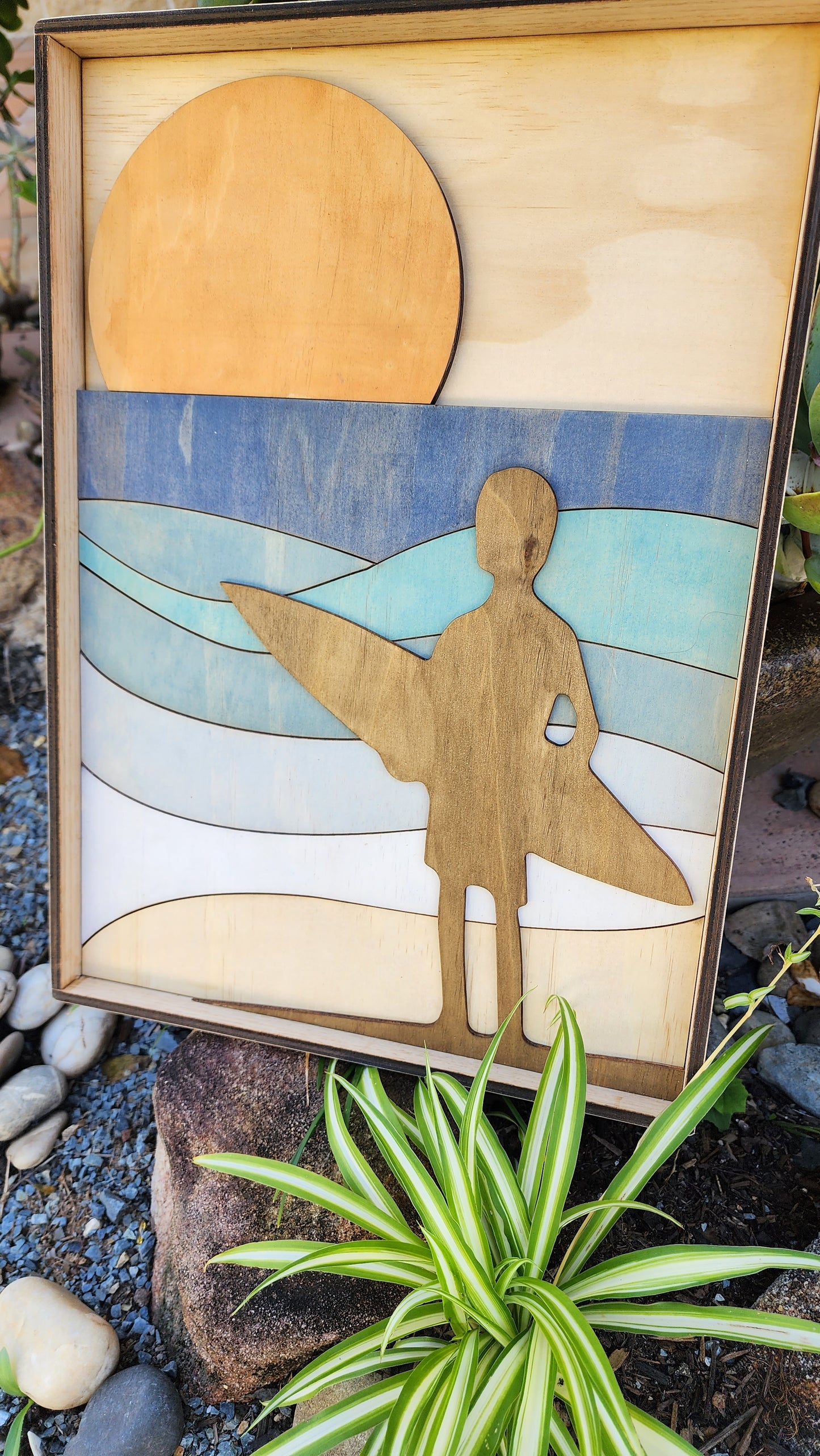 An artwork made from plywood featuring a silhouette of a surfer as they look out at the waves.